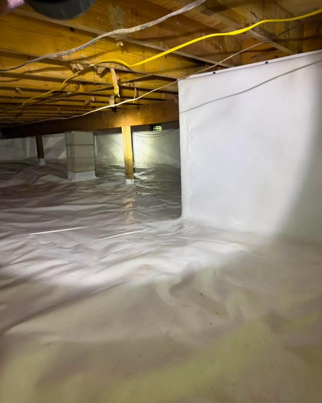 A crawl space sealed with a white vapor barrier.