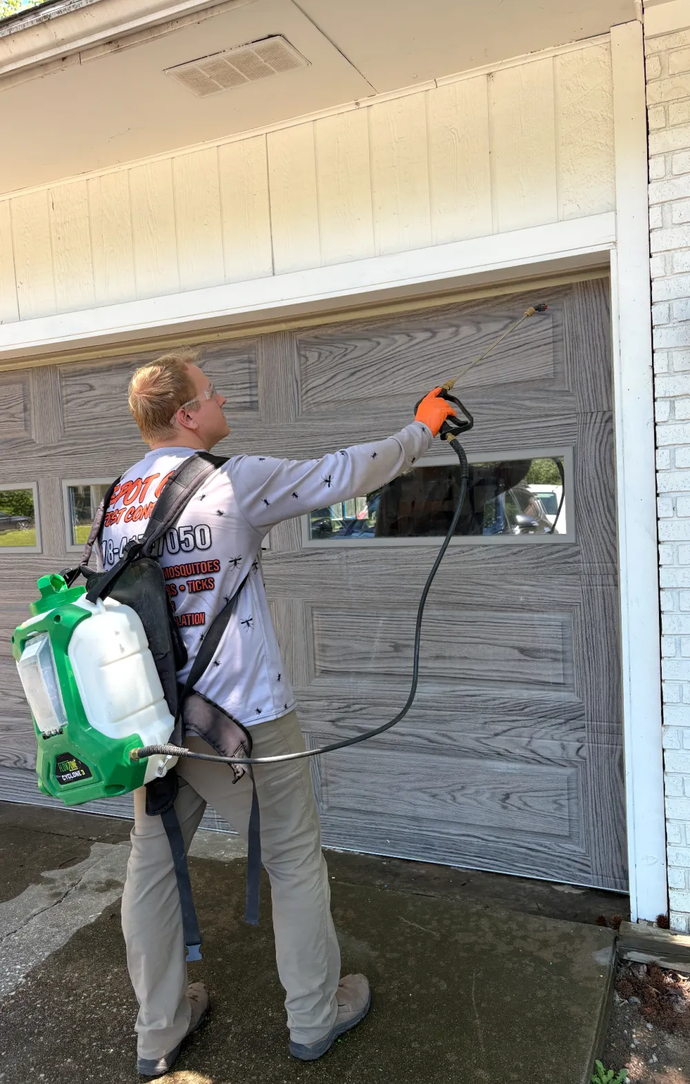 A Spot On technician with a backpack sprayer treating around a garage door.