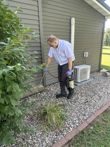A Spot On technician treating a landscaped bed beside a building.